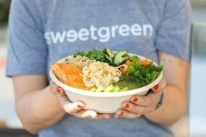 A woman with a sweetgreen shirt holding a salad bowl